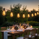 Outdoor dining setup with string lights and floral centerpieces in a garden.